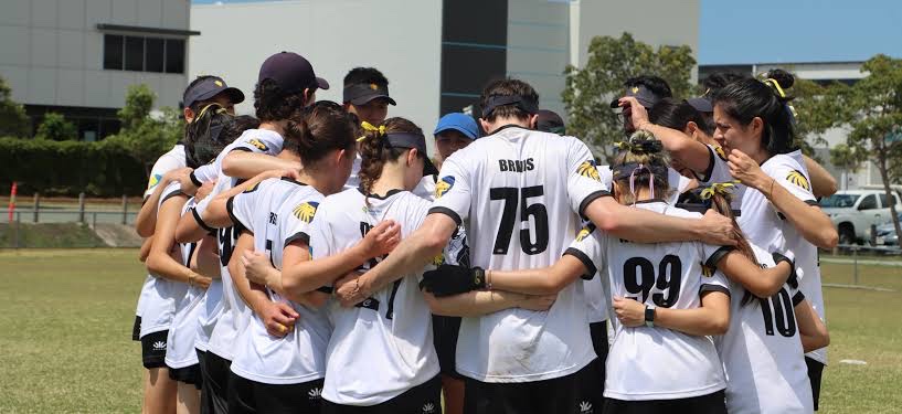 A sports team in white jerseys huddled together on the field before a match