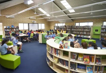 Primary school students reading in a bright library with curved green shelving