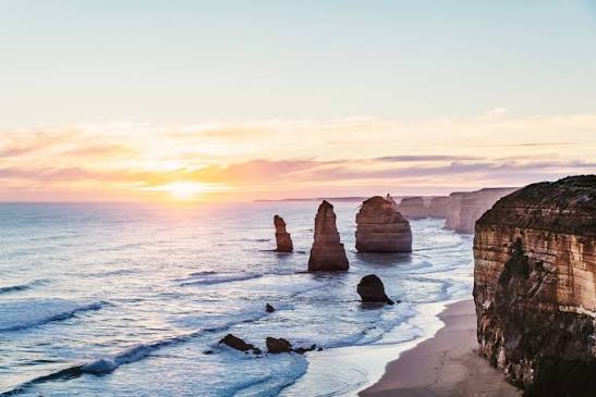 The Twelve Apostles on Victoria's Great Ocean Road at sunset, limestone stacks standing in the surf beside a cliff-lined beach