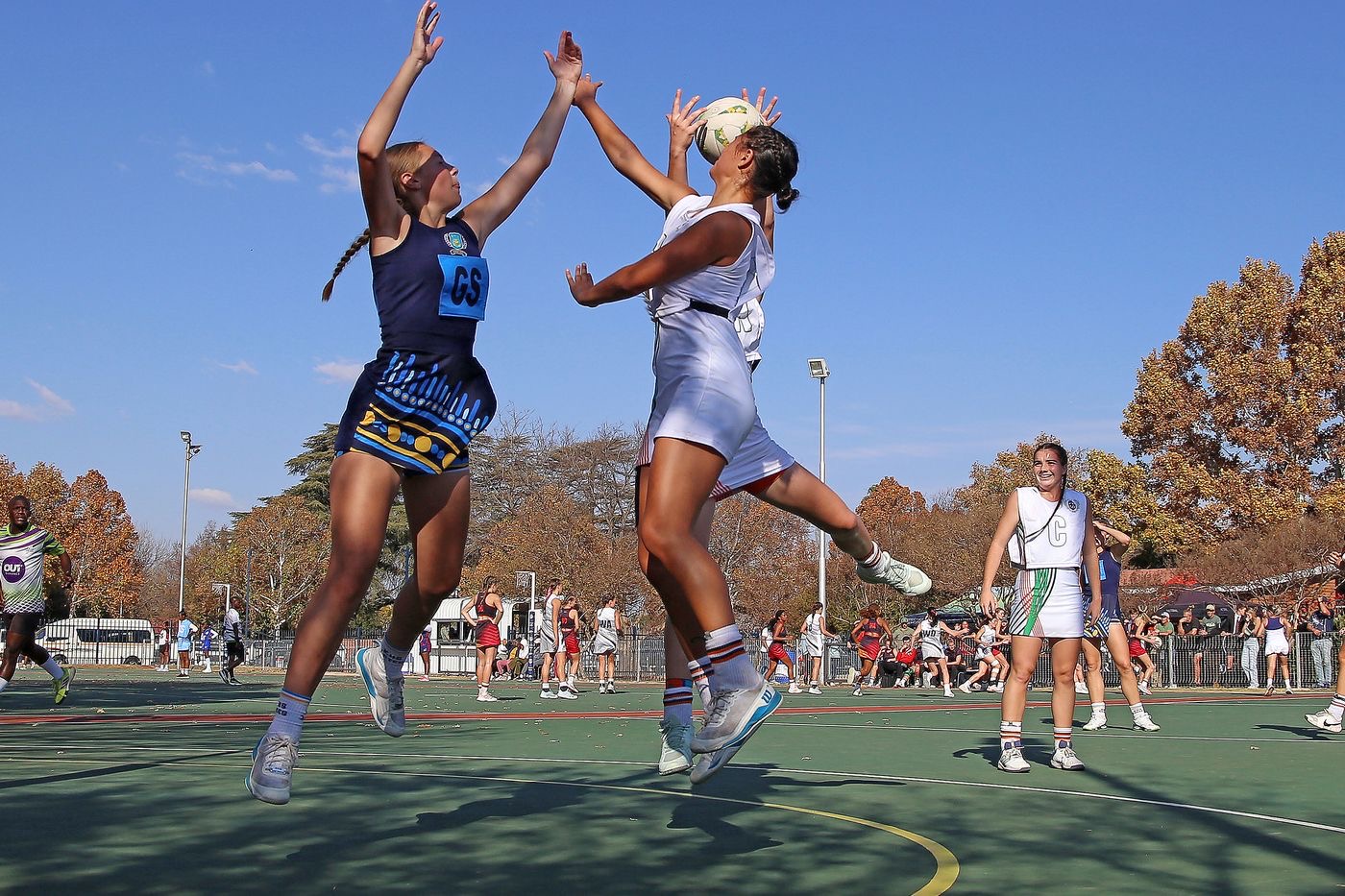 Two netball players leaping for the ball at an outdoor court on a sunny Saturday
